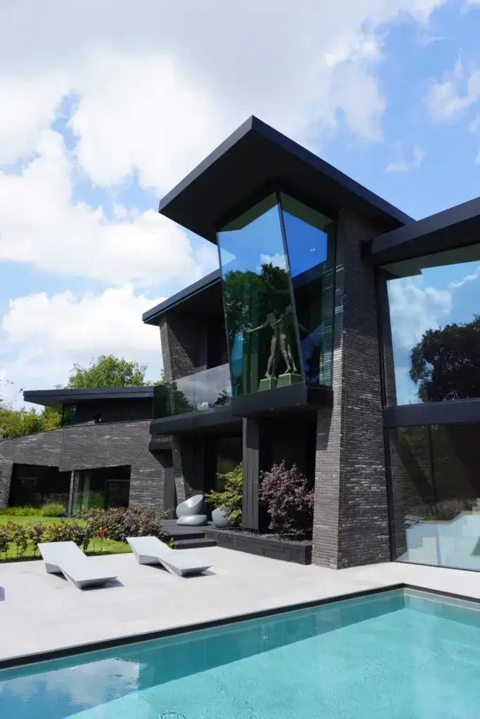Luxury modern residential property with dark brick exterior, expansive glazing and architectural surface detailing overlooking a private pool