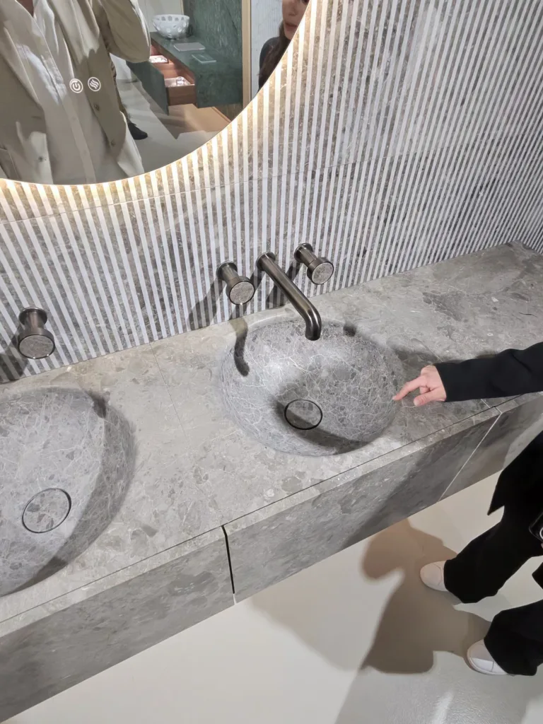 Twin sculpted marble basins by Luce di Carrara with brushed nickel taps against a fluted marble wall at Milan Design Week